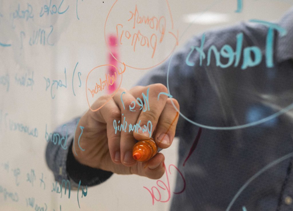 Person schreibt und brainstormt Ideen auf einem Glas Whiteboard.