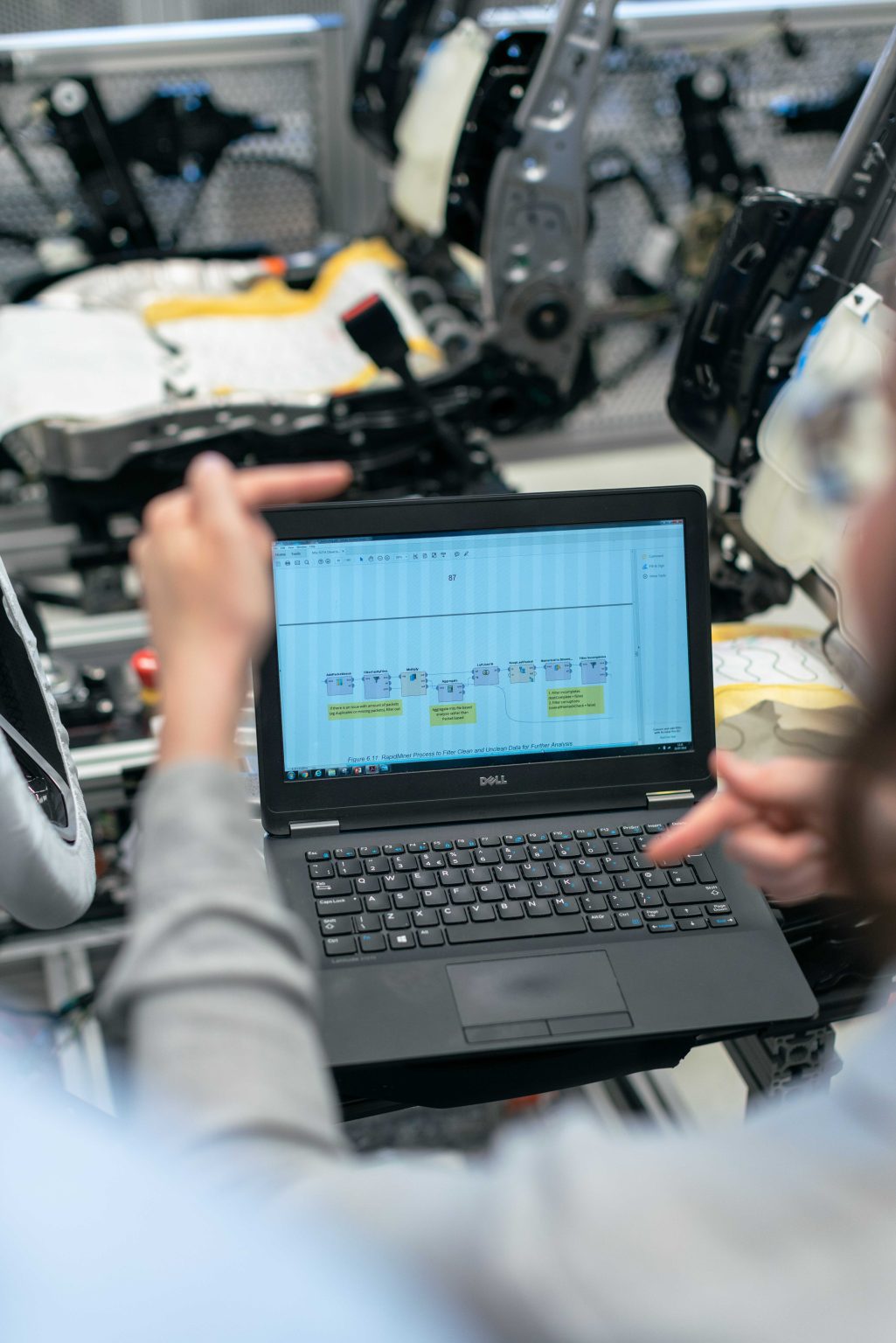 Ingenieur analysiert Produktionsdaten auf einem Laptop in einer Fabrikumgebung.
